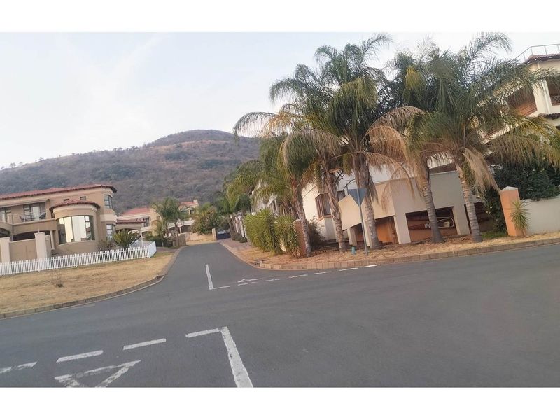 A view of the residential street and surrounding neighbourhood, featuring paved roads, established palm trees, and nearby residential properties with mountain views.