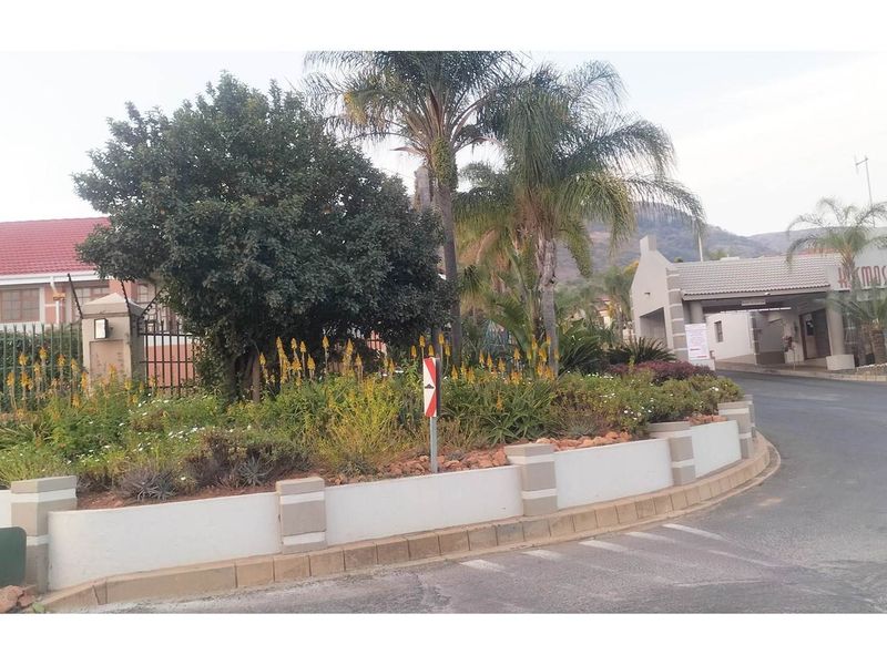 A view of the entrance and landscaped roundabout at the residential estate, featuring established trees and a paved road.