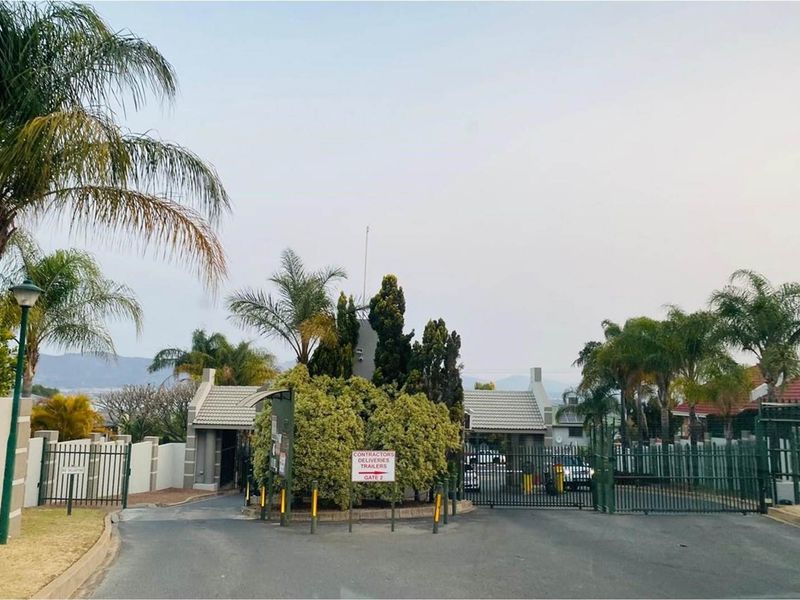 View of the secure gated entrance to the residential estate, featuring perimeter fencing, paved access road, and established landscaping.