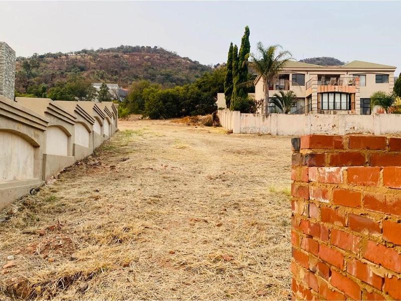 A vacant residential plot featuring established boundary walls, offering a clear building site with views of the surrounding landscape and neighboring properties.