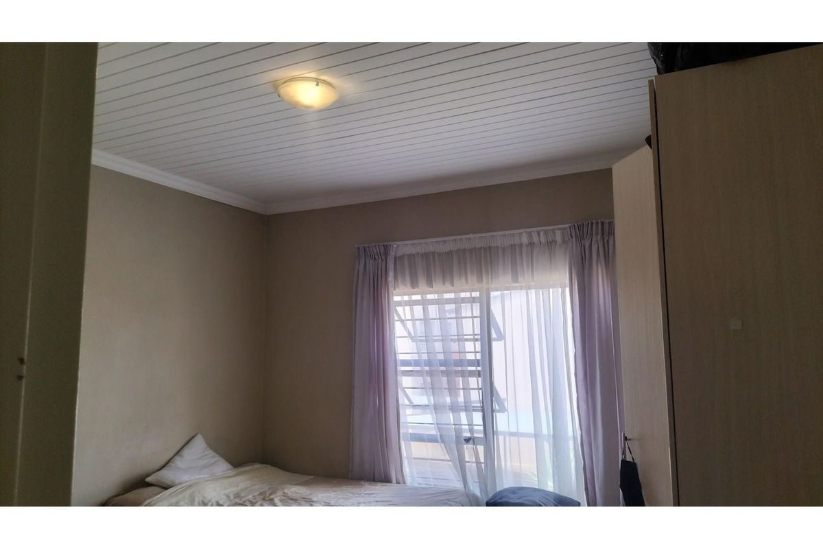 A bedroom featuring a white tongue-and-groove ceiling, built-in wardrobe, and a window with security bars.