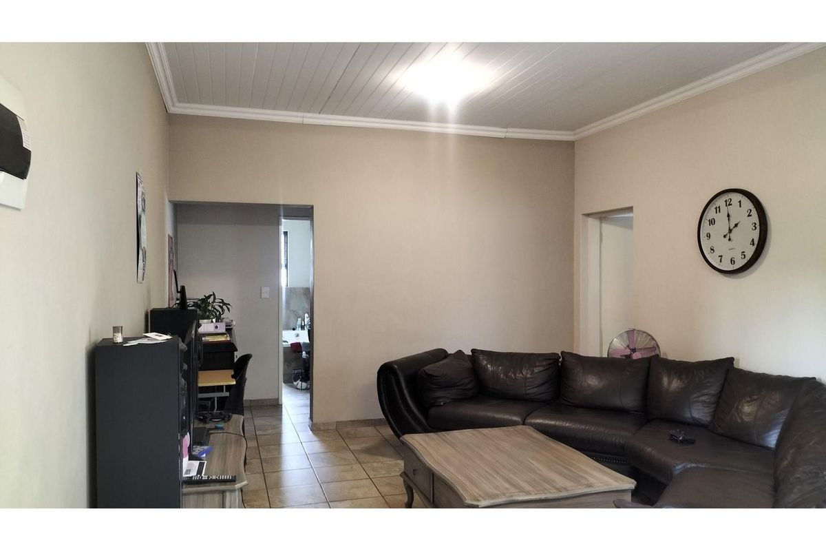 A living room featuring tiled flooring and a tongue-and-groove ceiling, with an adjacent hallway leading to a bathroom.