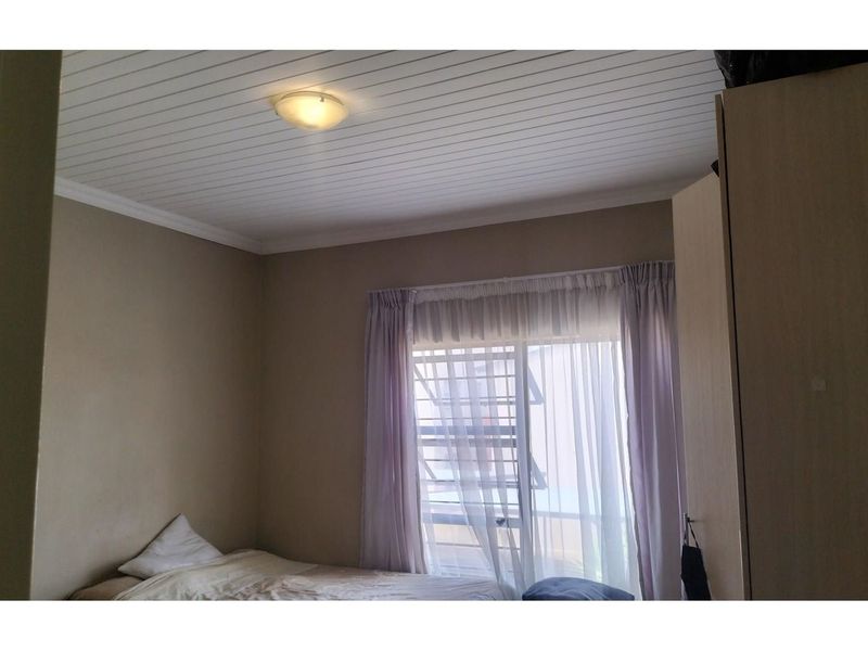 A bedroom featuring a white tongue-and-groove ceiling, built-in wardrobe, and a window with security bars.