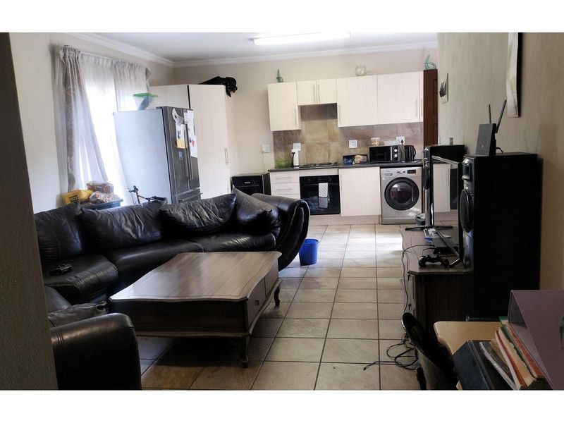 Open-plan living area featuring tiled flooring and a compact kitchen with built-in oven, hob, and integrated laundry appliance space.