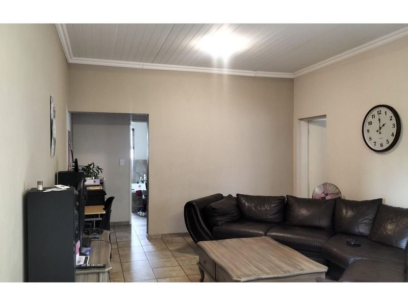 A living room featuring tiled flooring and a tongue-and-groove ceiling, with an adjacent hallway leading to a bathroom.
