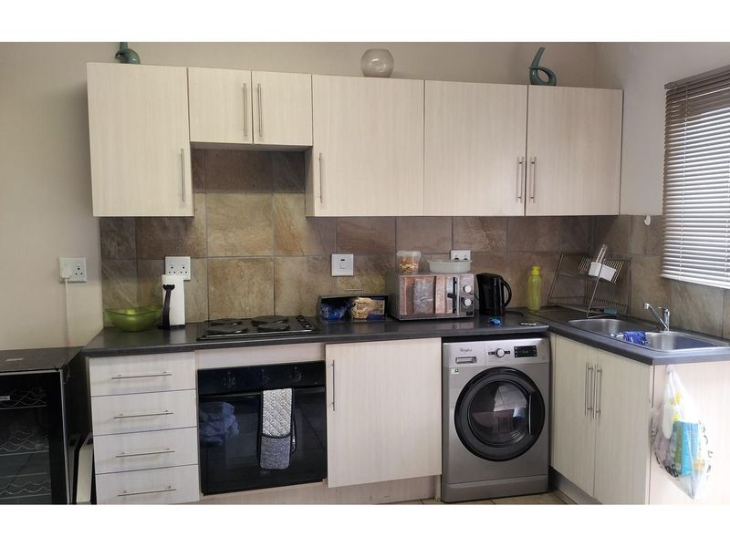 Compact kitchen featuring light wood-finish cabinetry, stone-look tiled backsplash, integrated oven, electric hob, and a built-in washing machine.