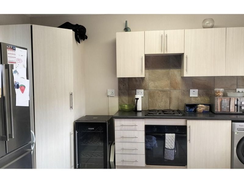 A functional kitchen featuring light wood-grain cabinetry, dark countertops, a built-in oven, hob, and integrated laundry appliance space.