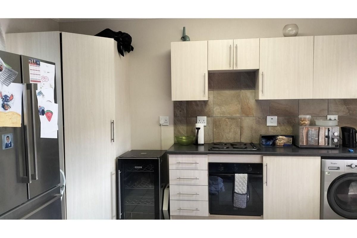 A functional kitchen featuring light wood-grain cabinetry, dark countertops, a built-in oven, hob, and integrated laundry appliance space.