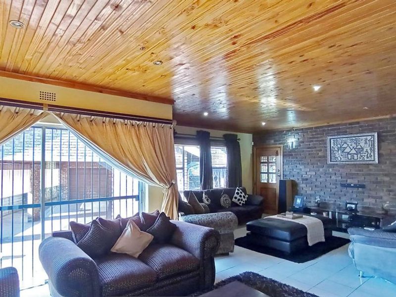 Spacious living room featuring a distinctive knotty pine wood-paneled ceiling, exposed brick feature wall, and large sliding glass doors leading to the exterior.