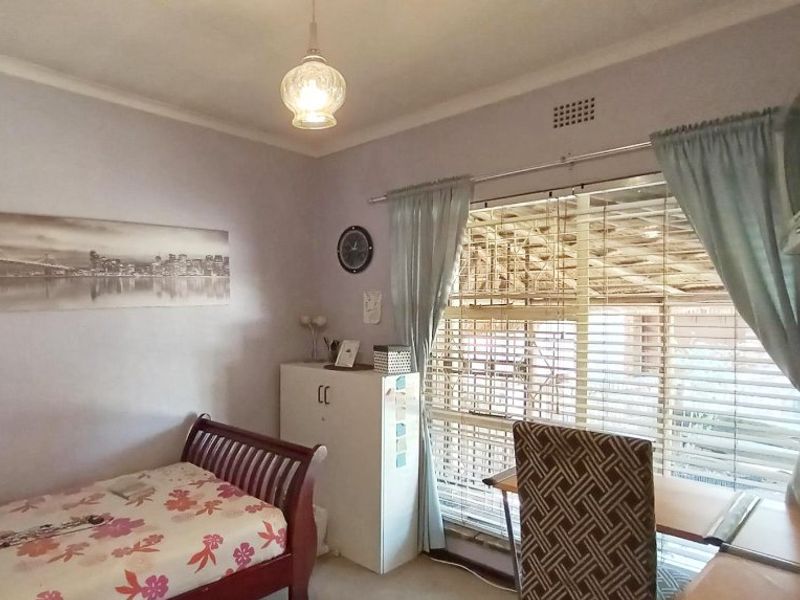 A functional bedroom featuring a window with fitted blinds and curtains, providing natural light and a view of the exterior structure.