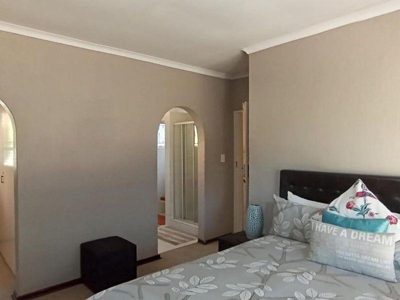A bedroom featuring arched doorways leading to an en-suite bathroom and a separate area, with neutral wall tones and coved ceiling detailing.