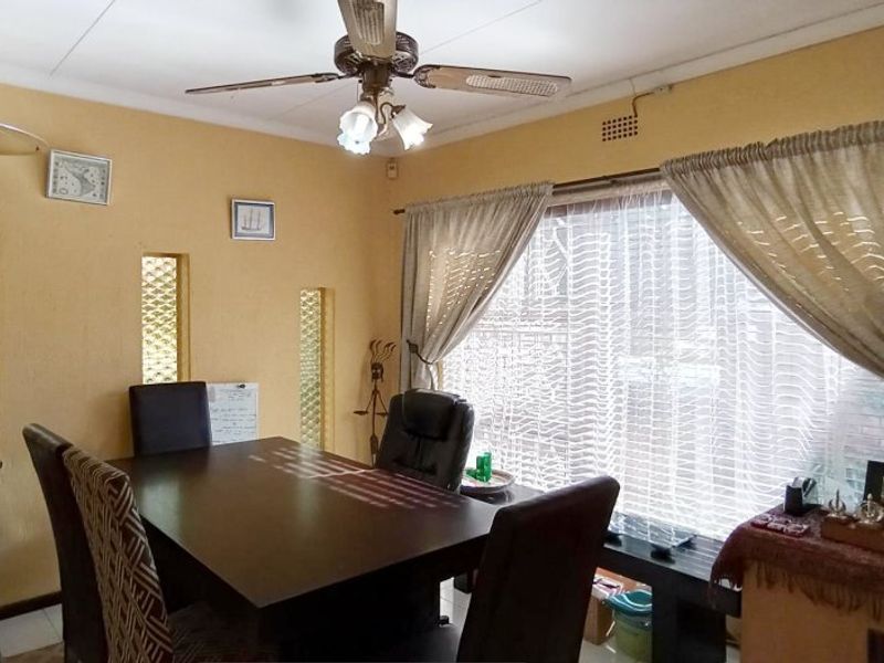 A dining room featuring textured walls, a ceiling fan, and large windows with curtains, providing a functional space for family meals.