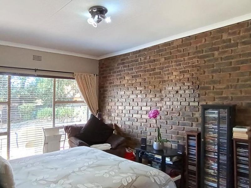 A bedroom featuring a prominent exposed brick feature wall, large windows with natural light, and a ceiling-mounted light fixture.