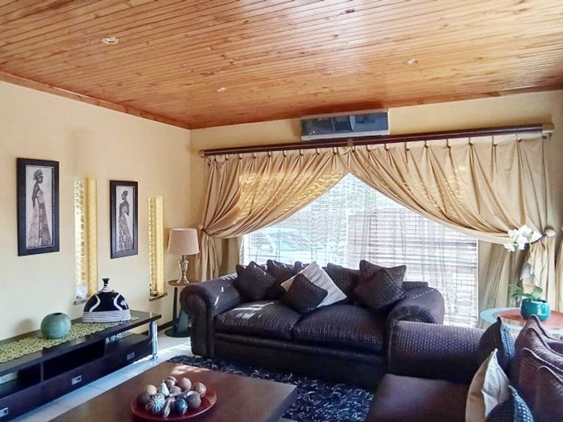 A cozy living room featuring a warm timber-paneled ceiling, recessed lighting, and a wall-mounted air conditioning unit.