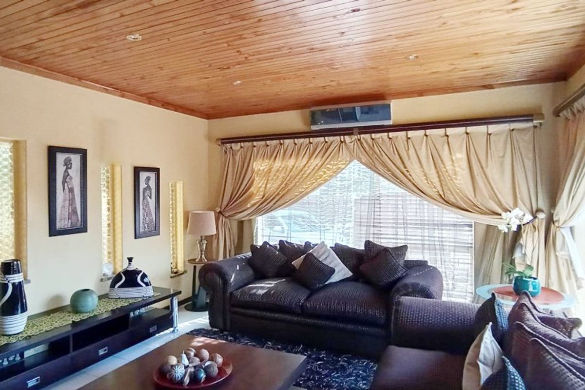 A cozy living room featuring a warm timber-paneled ceiling, recessed lighting, and a wall-mounted air conditioning unit.