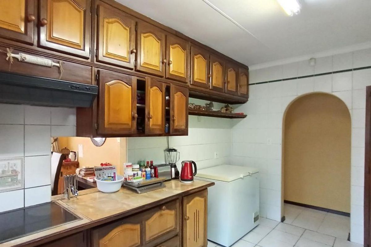 A dated kitchen featuring traditional wooden cabinetry, tiled splashbacks, and tiled flooring, with an arched doorway leading to an adjacent room.