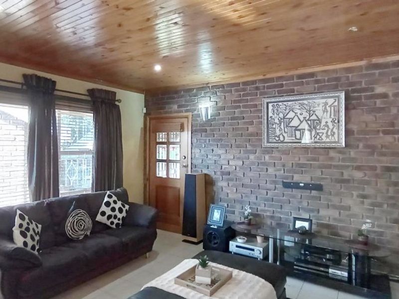 A living room featuring a prominent exposed brick feature wall, timber-clad ceiling, and tiled flooring, creating a warm and rustic atmosphere.