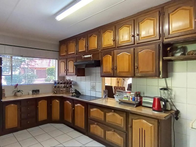 A functional kitchen featuring traditional timber cabinetry, tiled splashbacks, a built-in hob, and an extractor fan, offering a classic layout with ample storage space.