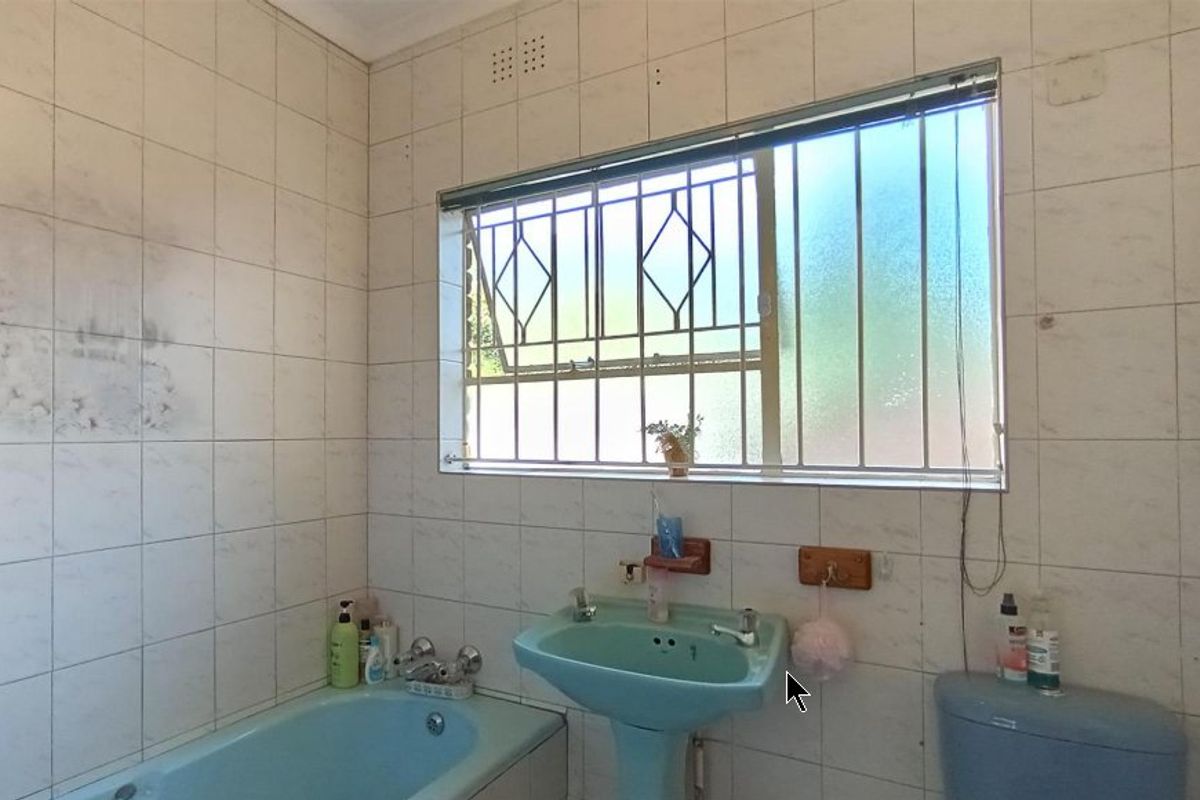 A dated bathroom featuring a blue bathtub and pedestal basin, tiled walls, and a window with security bars.