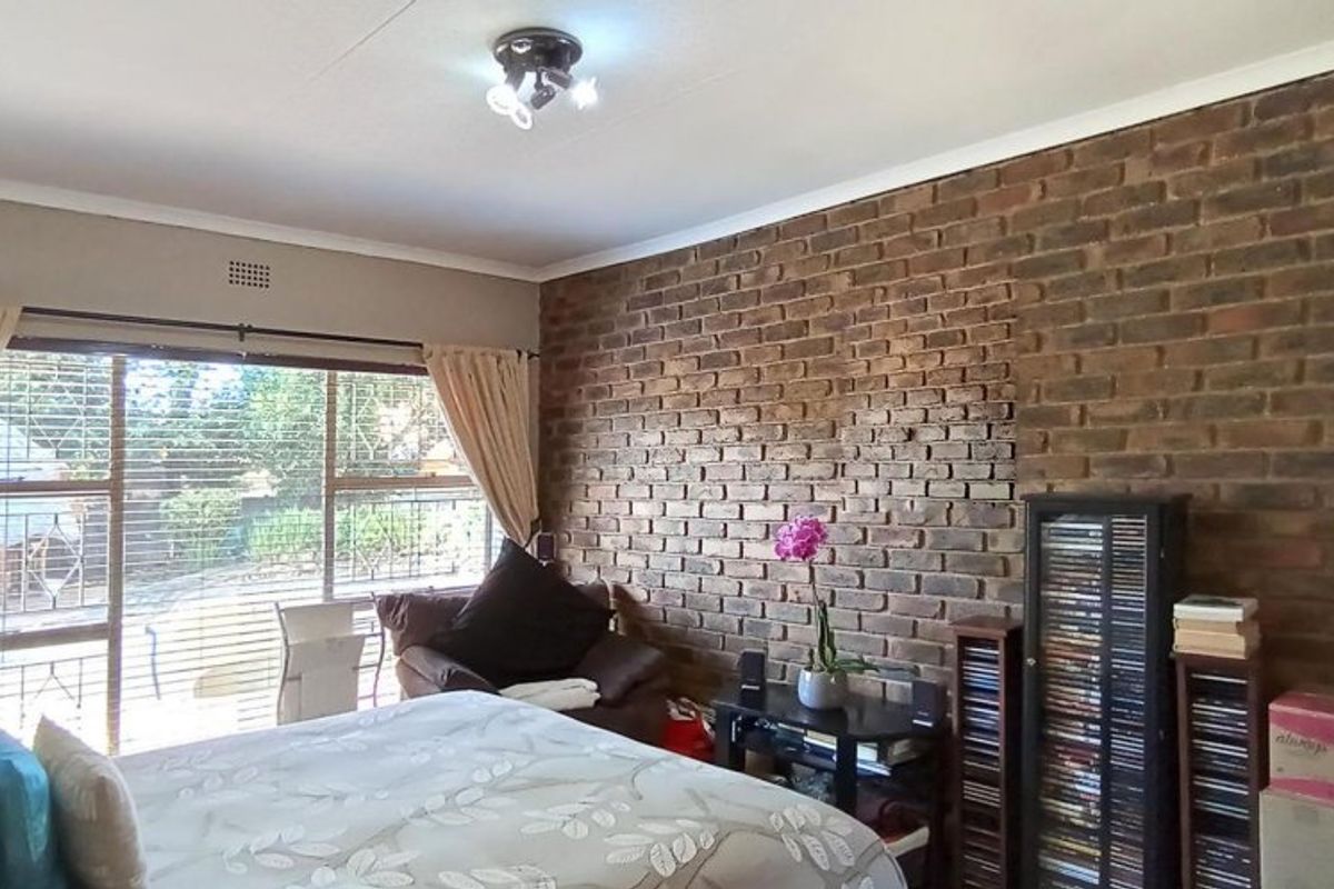 A bedroom featuring a prominent exposed brick feature wall, large windows with natural light, and a ceiling-mounted light fixture.
