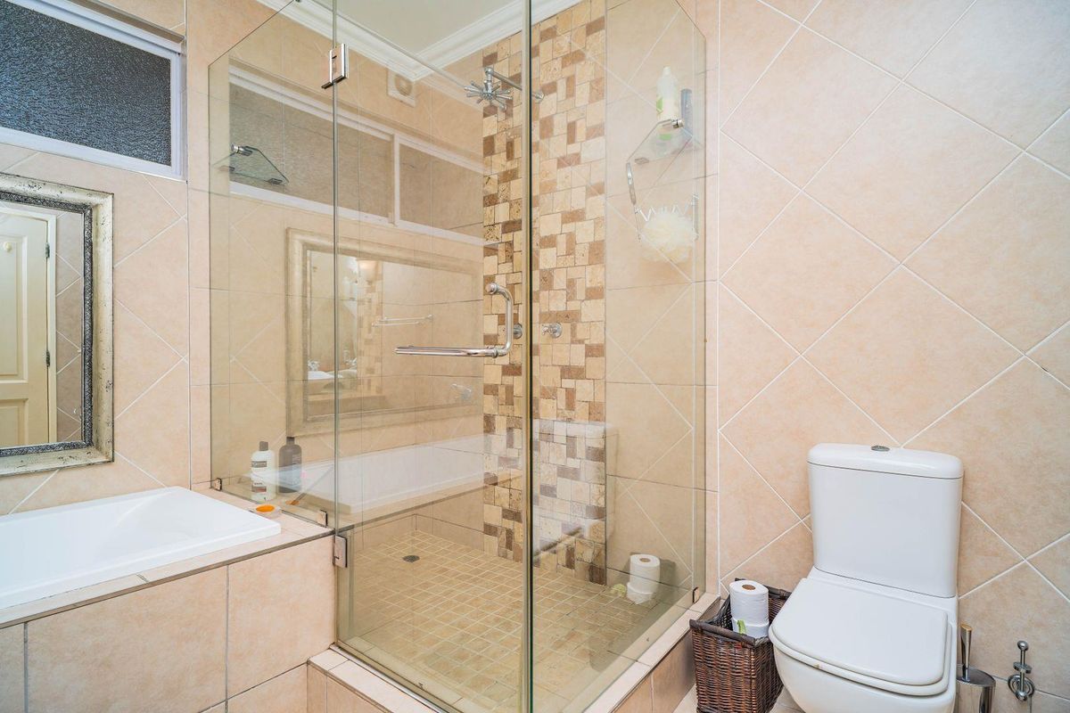A well-maintained bathroom featuring a glass-enclosed shower, built-in bathtub, and neutral ceramic tiling with a decorative mosaic accent wall.