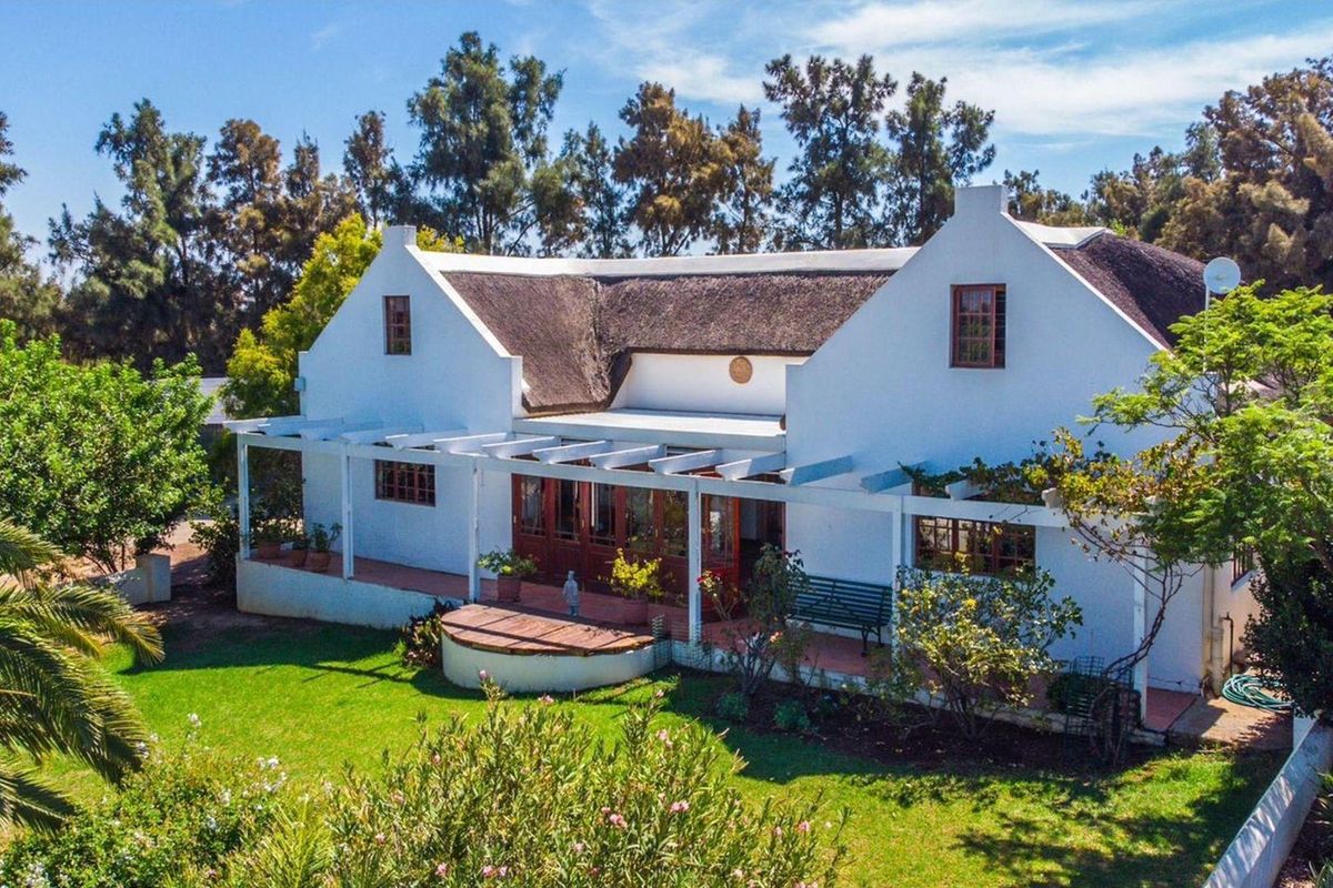 A charming farmhouse featuring a traditional thatched roof, a covered pergola patio, and well-maintained garden surroundings.