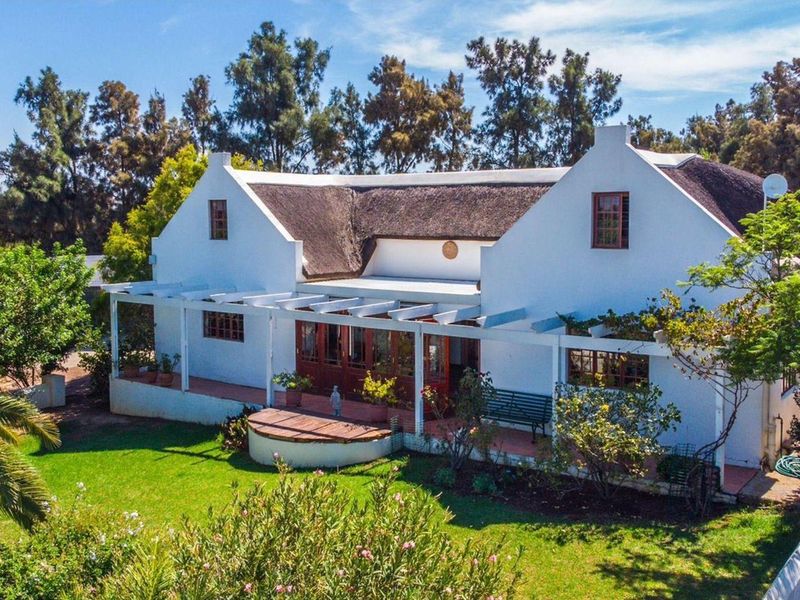 A charming farmhouse featuring a traditional thatched roof, a covered pergola patio, and well-maintained garden surroundings.
