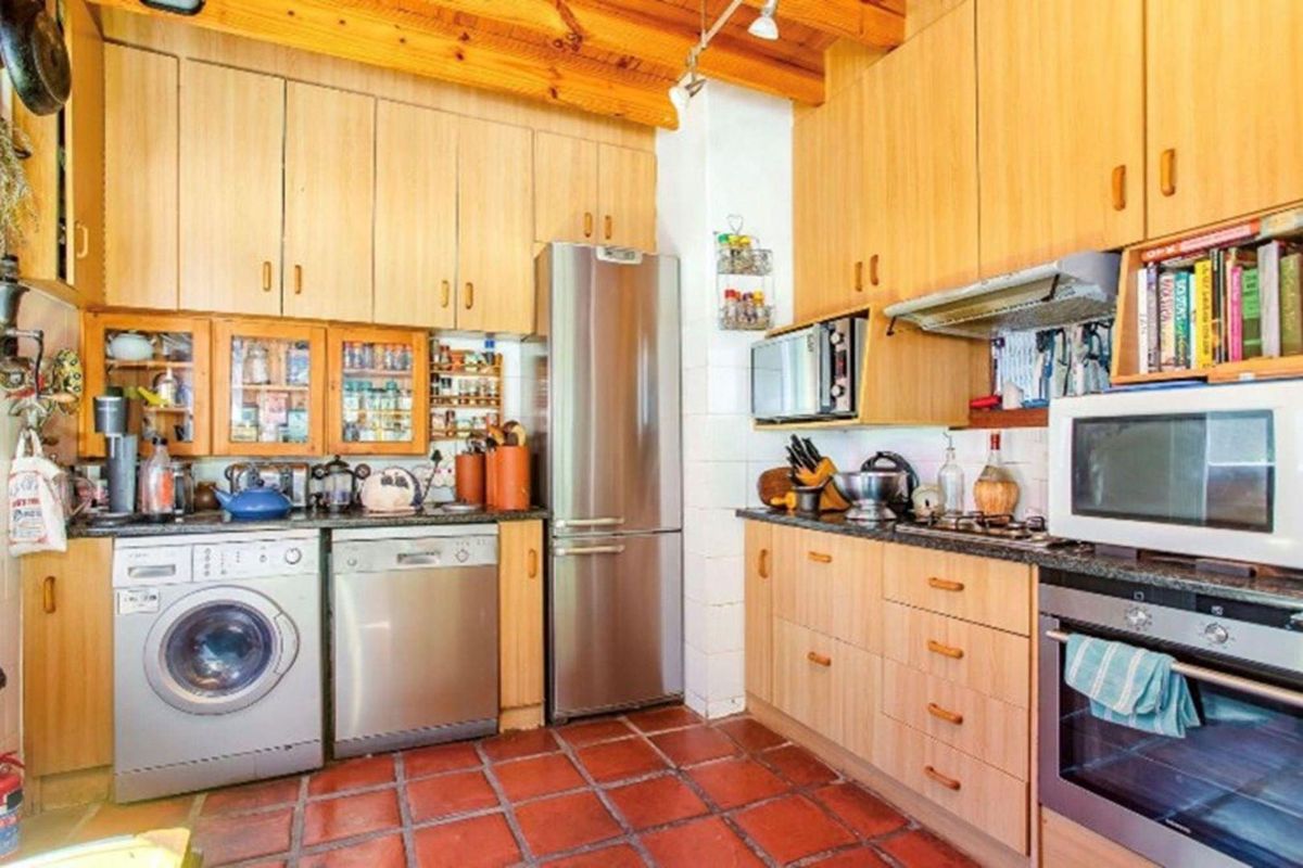 A functional kitchen featuring light wood cabinetry, granite countertops, exposed timber ceiling beams, and terracotta floor tiles, equipped with integrated stainless steel appliances.