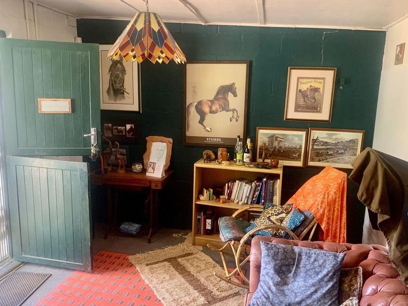 A rustic living area featuring dark green painted blockwork walls, a traditional stable door, and a unique pendant light fixture.