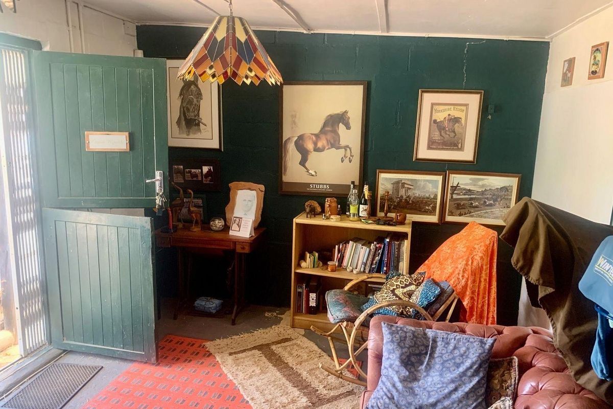 A rustic living area featuring dark green painted blockwork walls, a traditional stable door, and a unique pendant light fixture.