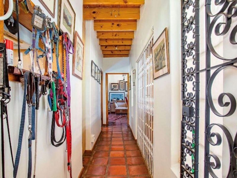 A rustic hallway featuring exposed timber ceiling beams, traditional terracotta floor tiles, and a decorative wrought iron security gate.