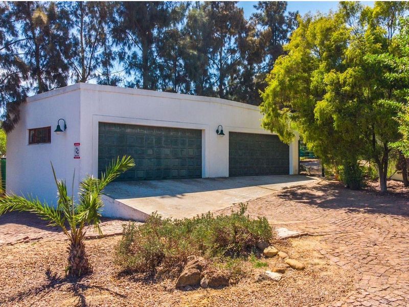 A detached double garage with a concrete driveway, set within a landscaped farm property with mature trees.