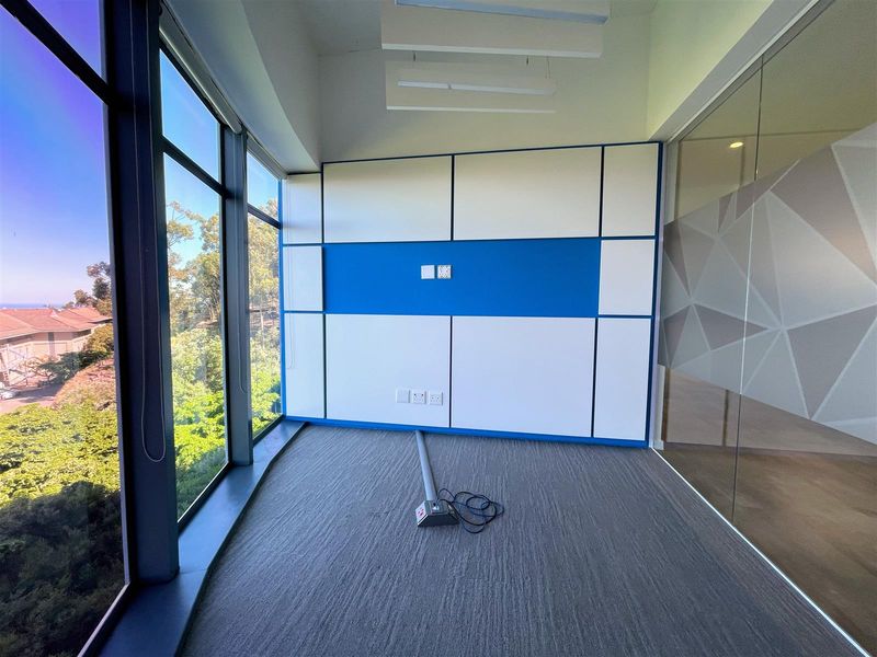 A bright, modern office space featuring floor-to-ceiling windows with scenic views, glass partitioning, and contemporary built-in wall paneling.