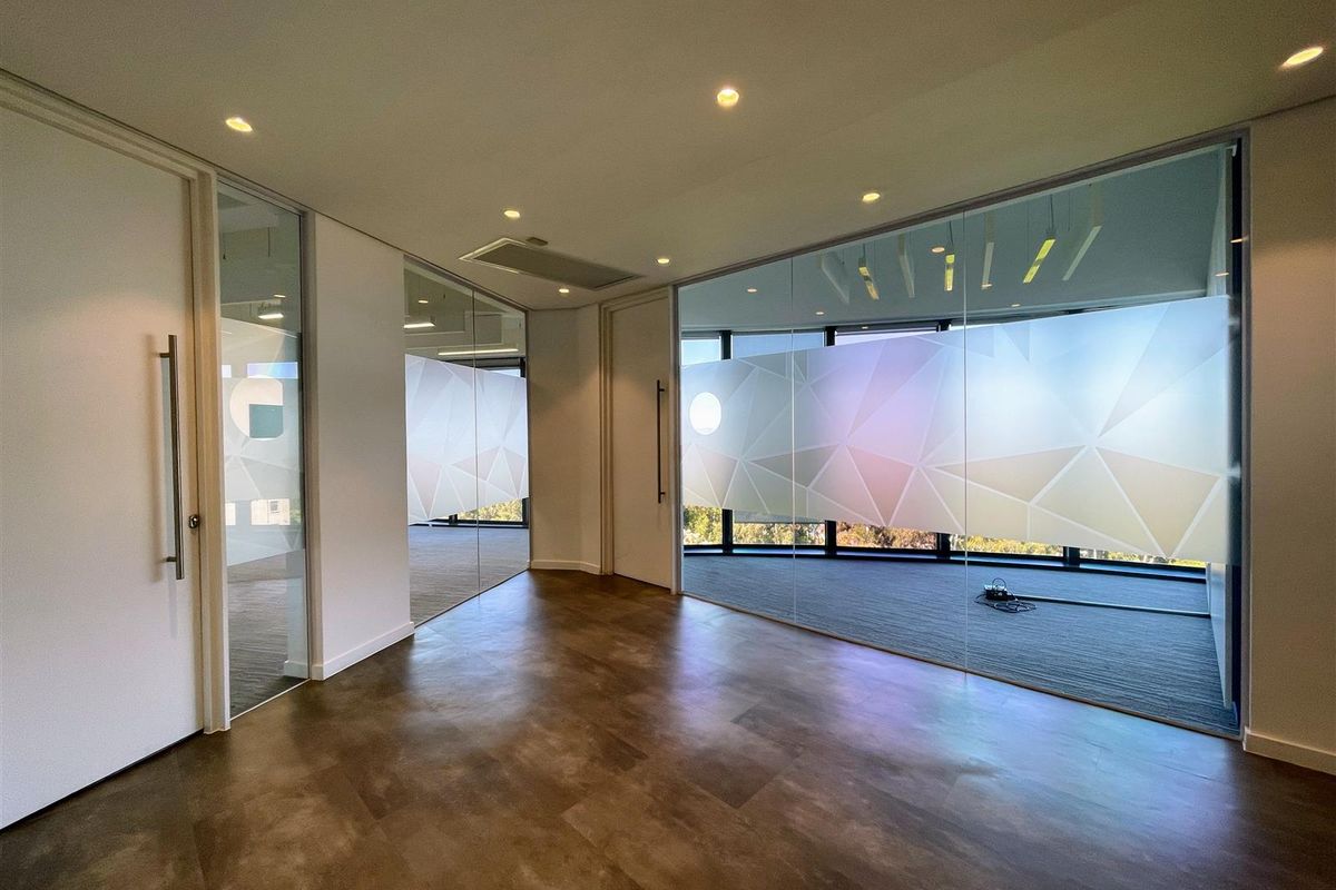 Modern office space featuring glass partition walls, recessed lighting, and high-quality vinyl flooring, offering a bright and professional work environment.