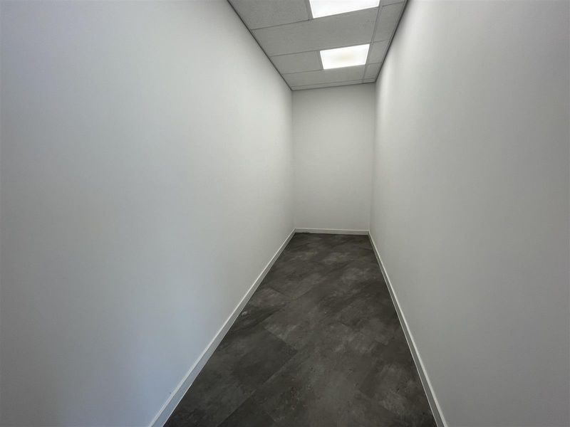 A clean, empty office space featuring modern vinyl flooring, white walls, and a suspended ceiling with recessed lighting.