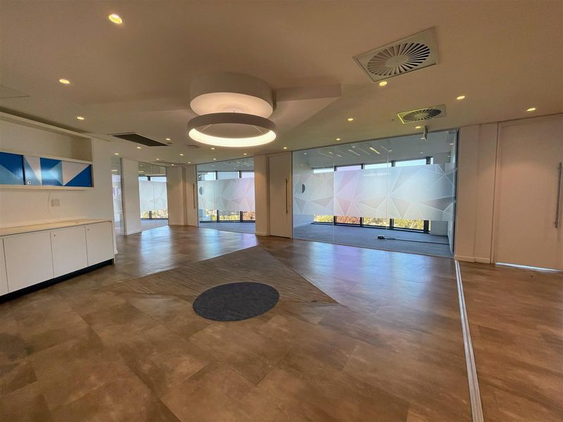 Modern open-plan office space featuring glass partitions, built-in cabinetry, recessed lighting, and large windows with frosted privacy film.
