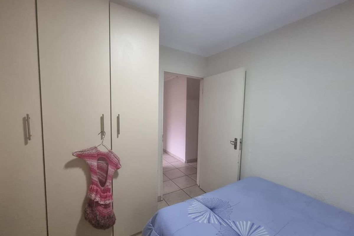 A bedroom featuring built-in wardrobes and tiled flooring, providing a functional space with direct access to the hallway.