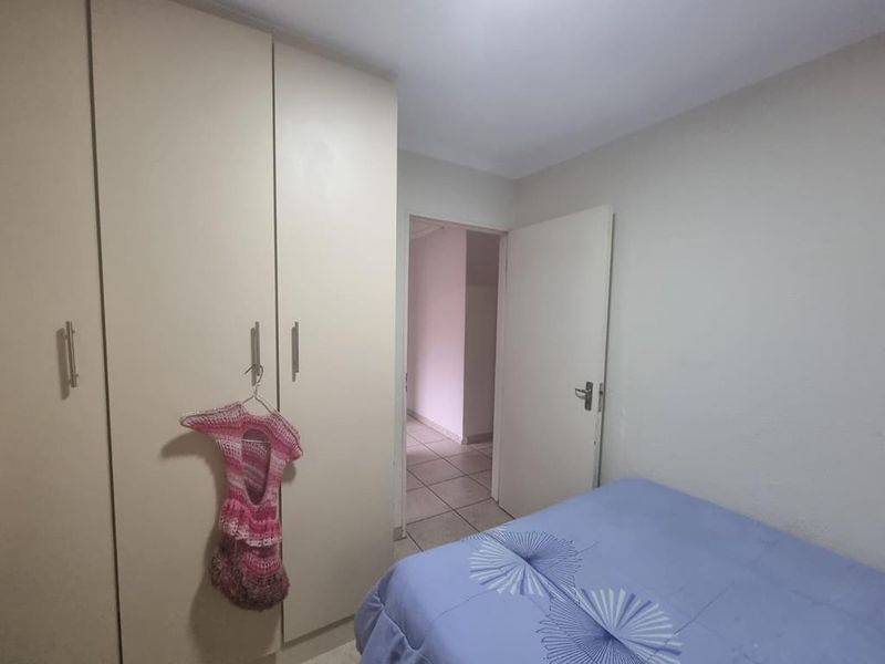 A bedroom featuring built-in wardrobes and tiled flooring, providing a functional space with direct access to the hallway.