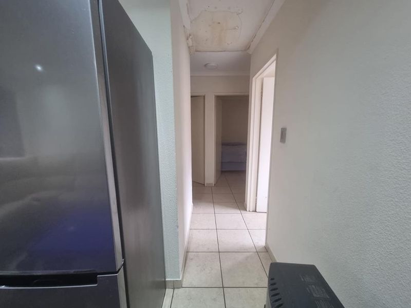 A narrow hallway with tiled flooring showing visible ceiling water damage and peeling paint, requiring maintenance and repair.