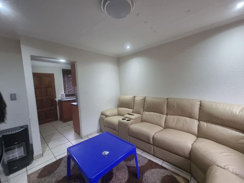 A living room area featuring tiled flooring and recessed ceiling lighting, with a clear transition into the adjacent kitchen space.