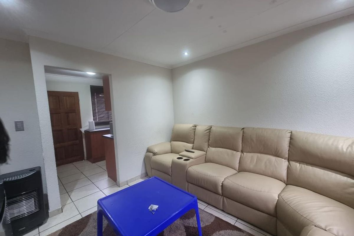 A living room area featuring tiled flooring and recessed ceiling lighting, with a clear transition into the adjacent kitchen space.
