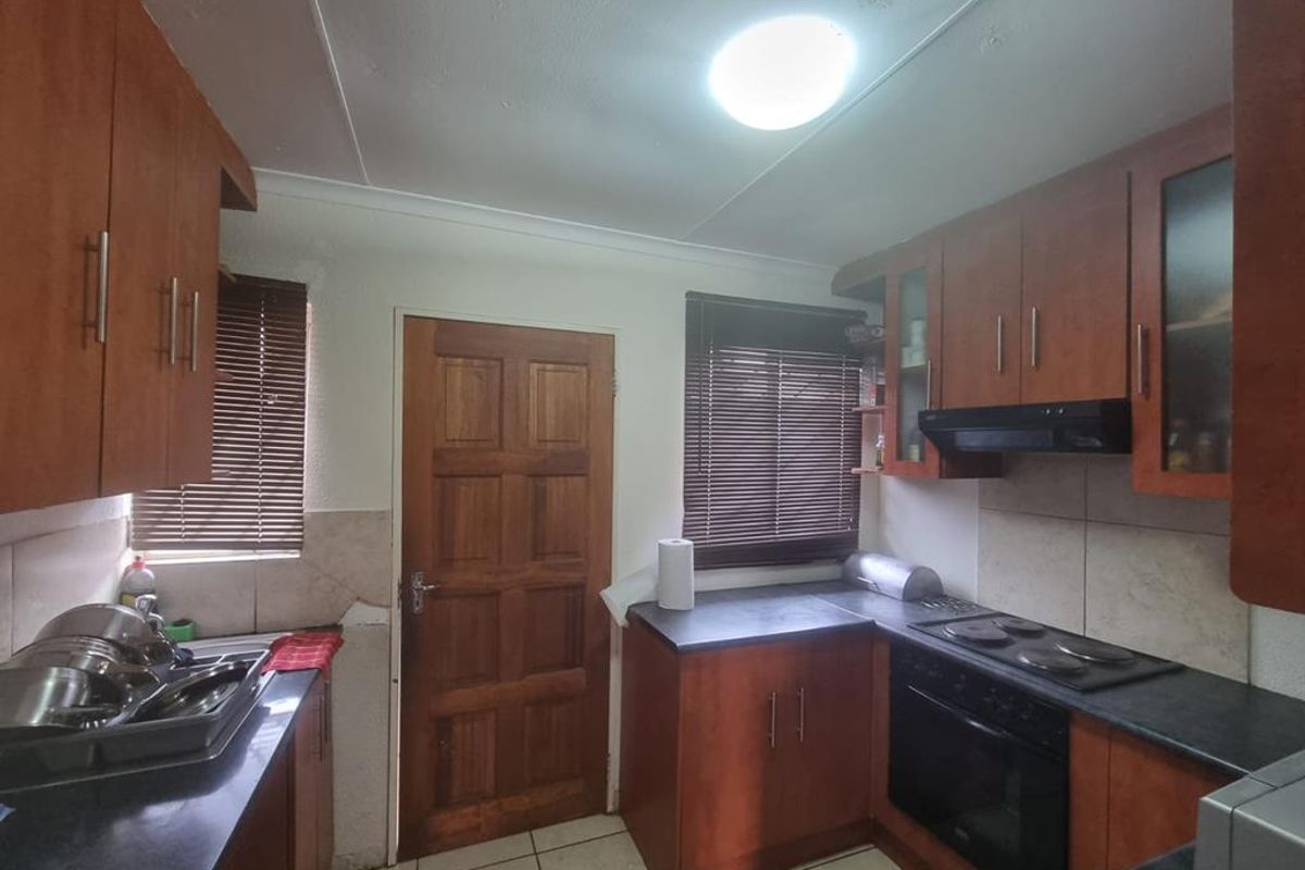 A functional kitchen featuring wood-finish cabinetry, dark laminate countertops, built-in electric oven and hob, and tiled flooring with direct exterior access.