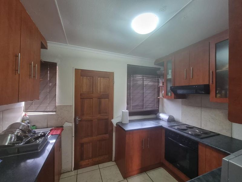 A functional kitchen featuring wood-finish cabinetry, dark laminate countertops, built-in electric oven and hob, and tiled flooring with direct exterior access.