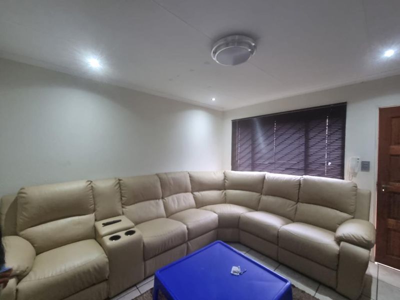A living room featuring tiled flooring, venetian blinds, and recessed lighting. The space includes an intercom system and shows minor ceiling water staining.