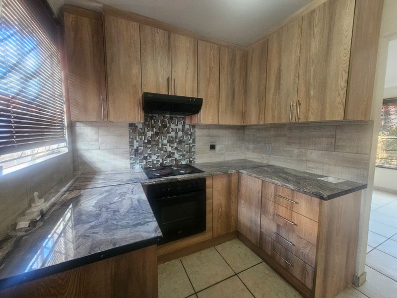 A functional kitchen featuring wood-look cabinetry, stone-patterned countertops, built-in oven and hob, and a decorative mosaic tile backsplash.