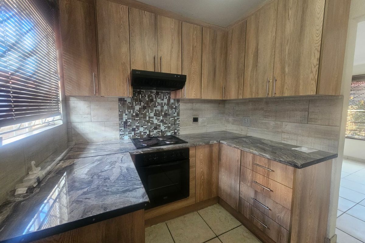 A functional kitchen featuring wood-look cabinetry, stone-patterned countertops, built-in oven and hob, and a decorative mosaic tile backsplash.