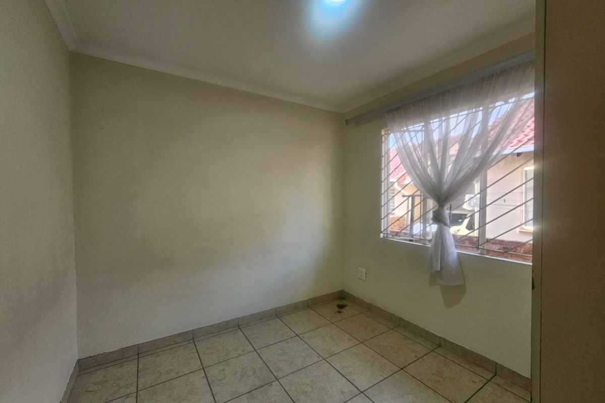 An empty bedroom featuring tiled flooring, security bars on the window, and neutral wall finishes, offering a blank canvas for personalization.