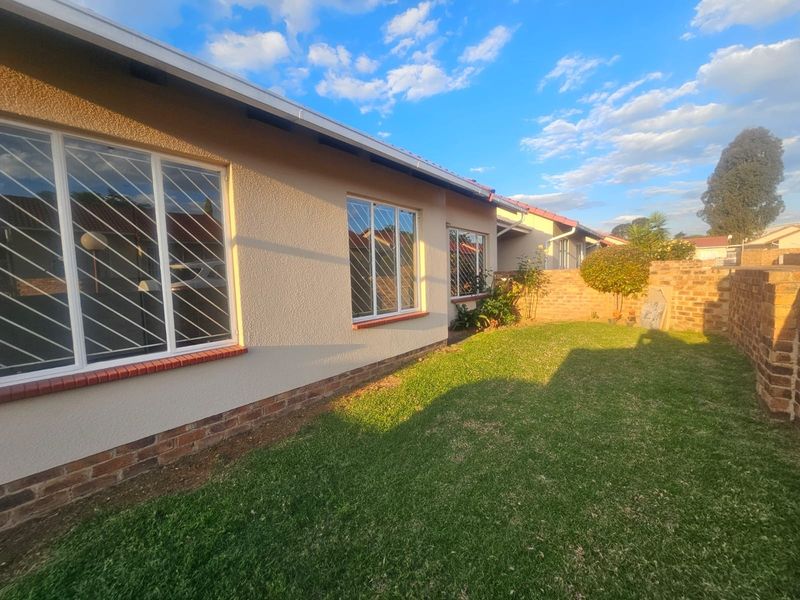 Rear view of the townhouse featuring a well-maintained lawn, textured stucco exterior walls, brick detailing, and secure window bars.