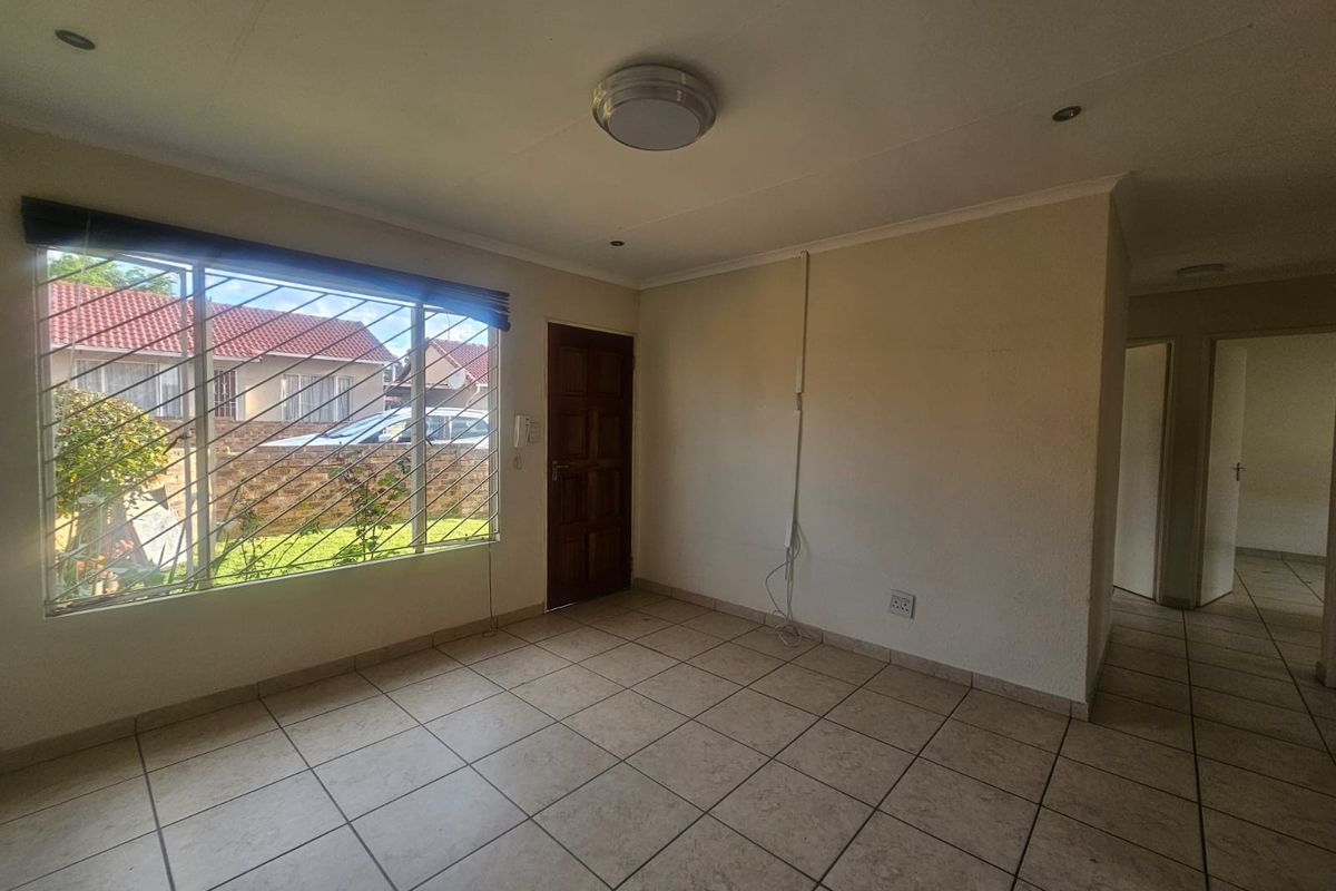 An empty living area featuring tiled flooring, a large window with security bars, and an intercom system, ready for personalization.