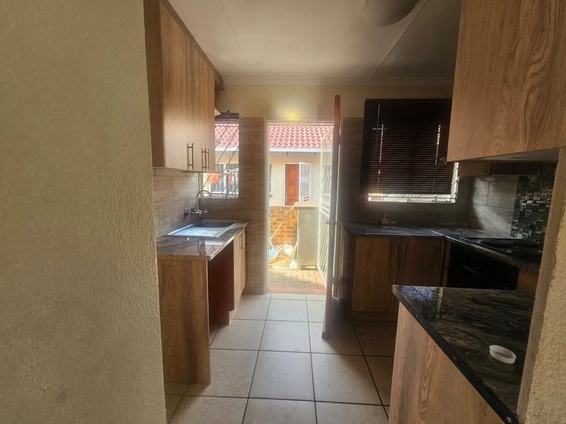 A functional kitchen featuring wood-look laminate cabinetry, granite countertops, and tiled flooring, with direct access to an outdoor area.